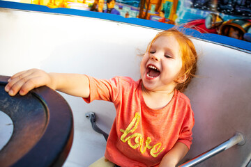 a little red-haired girl on the attraction laughs and enjoys the ride