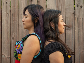 Fototapeta premium Twin sisters standing back to back with a wooden fence background