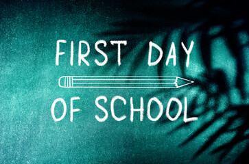 Fototapeta premium First Day of School greeting card. Text on school chalkboard with palm leaves shadows. Back to school concept, mixed media.