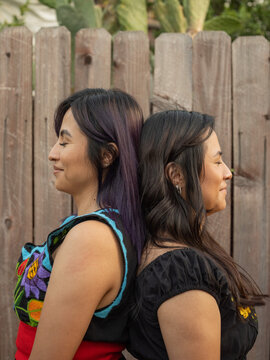 Portrait of twin sisters with their eyes closed standing back to back