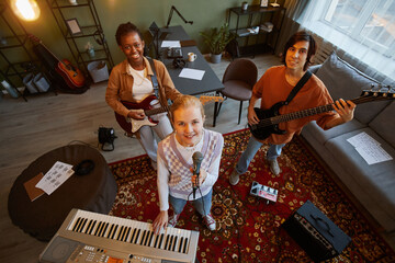 High angle portrait of music band practicing in home studio with focus on young blonde woman holding microphone and looking up at camera