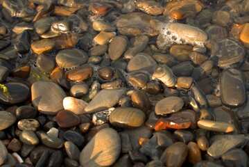 A pure transparent sea wave rolls over the rocky pebble shore, the concept of rest and travel, tranquility, relaxation and reflection on a warm summer day, close-up.