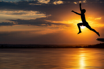 Weiter Sprung eines jungen in einen See mit Sonnenuntergang im Hintergrund