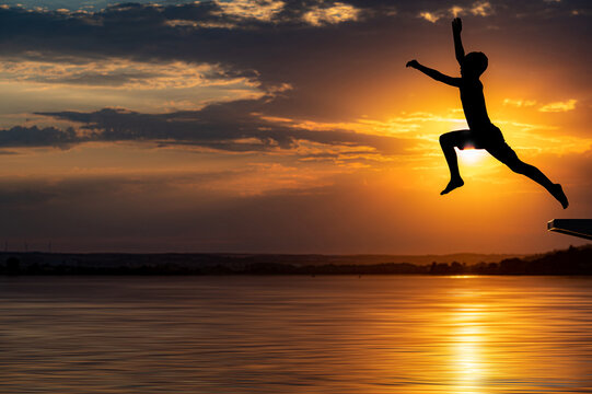 Weiter Sprung eines jungen in einen See mit Sonnenuntergang im Hintergrund