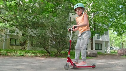 The girl in the blue helmet rides a scooter along a European city street on a summer sunny day