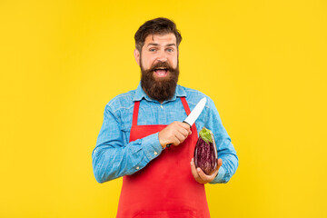 Excited man in apron holding chefs knife and eggplant yellow background, chef