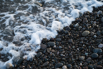 Close-up of small stones on pebbled beach. Sea foam.