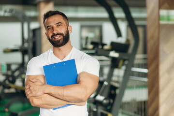 Portrait of personal trainer holding clipboard with training plan in gym