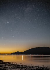 Vertical shot of a starry night and a beach with boats on the water and hills afar during sunset