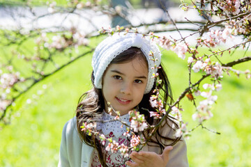 Portrait of a little girl in the flowering branches of a spring tree