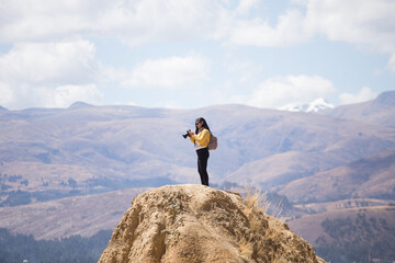 Mujer turista tomando fotos con una cámara profesional desde lo alto de una montaña con montañas alrededor. Concepto de personas, estilos de vida, turismo y aventura.