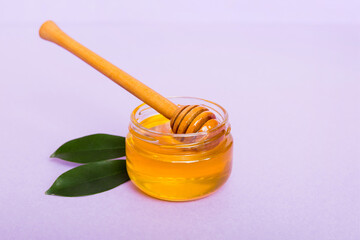 Honey in jar with leaves and honey dipper on colored background top view with copy text