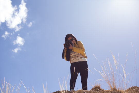 Mujer Fotógrafa Haciendo Fotos Con El Cielo Azul De Fondo. Concepto De Profesiones, Turismo, Viajes, Aventura Y Personas.