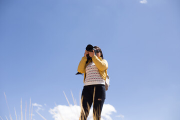 Mujer fot&oacute;grafa haciendo fotos con el cielo azul de fondo. Concepto de profesiones, turismo, viajes, aventura y personas.