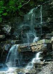 Vertical shot of the beautiful Issaqueena Falls streaming down rocks in a forest on a sunny day - obrazy, fototapety, plakaty