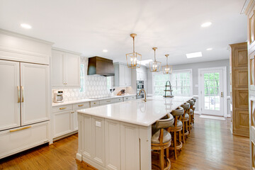 Luxury interior staged kitchen white stone countertops decor stools ceramic tile backsplash modern brass light pendants wood columns