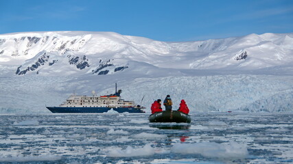 Zodiac inflatable boat navigating among icebergs, away from an expedition cruise ship, in Cierva Cove, Antarctica