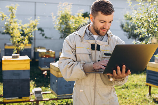 Male agronomist or engineer in protective suit working on laptop at bee farm