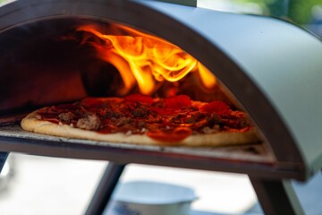 Closeup shot of a crusty pizza cooking in an outdoor oven in a garden