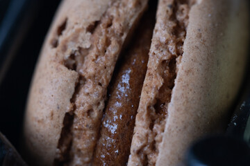 Close-up of flavourful brown macaron on black background. Sweet concept. Excellent image for dessert banners and advertisements. 