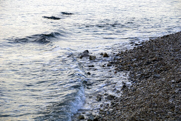 The silvery surface of the sea water that washes over the pebbly seashore