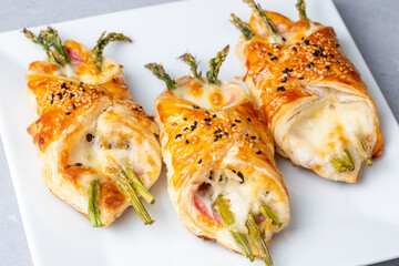 Baked green asparagus with ham and cheese in puff pastry sprinkled with sesame seeds and green basil leaves.