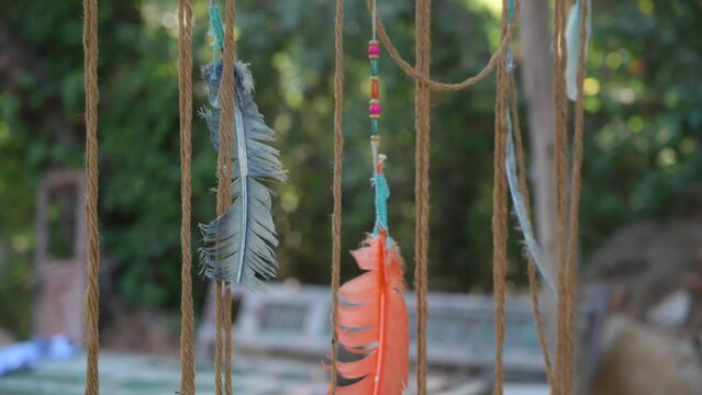 Closeup shot of feathers and strings on dreamcatcher with trees in the background