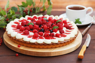 Summer berry pie with cheese cream on a wooden board with a cup of tea.