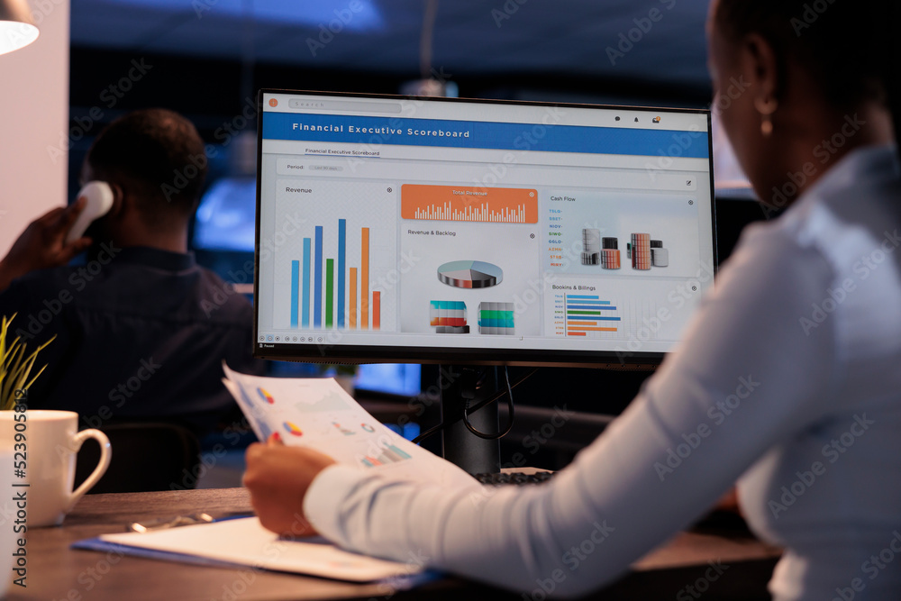 Poster office employee analyzing business charts on computer and documents, looking at online research data