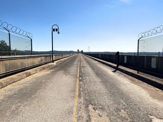 Road with fence with concertina razor wires under the blue sky - prison walls