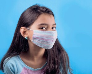 Little funny girl with a colorful mask. Excitement and fascination concept. Close-up portrait. Coronavirus blue background. foolish grimaces comical crazy gestures. Funny expression. Stop Covid-22. 