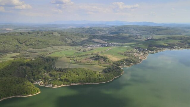 Aerial view of a lake surrounded  by dense green forests and the buildings on the coast