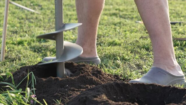 Man using tools hand-held soil hole drilling machine or portable manual earth auger for prepare the soil for planting trees. autumn work in the garden, building a fence