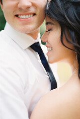 Bride touches her forehead to the cheek of the smiling groom. Cropped
