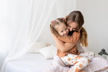 Happy loving family. Mother and her daughter girl play and have fun on the bed in the bedroom. The pleasure of being a mom, mother's day greetings, the concept of a sweet moment together