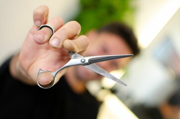 Selective focus of a man cutting with silver metal scissors