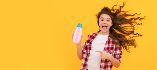 happy teen girl with long curly hair hold shampoo bottle, fun. Banner of child girl hair care, studio poster header with copy space.