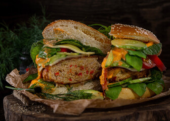 hamburger with juicy cutlet, cut in half with vegetables, on paper, lying on a wooden table on a dark brown background