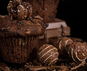 Delicate chocolate cupcakes with milk chocolate, with round chocolates and crumbs. On a black background.