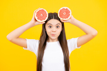 Teenage girl holding a grapefruit on a yellow background. Funny face.