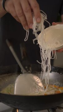 Vertical close-up of a man adding funchosa to a pan