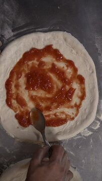 Vertical view of a chef putting tomato sauce on the fresh pizza dough in the restaurant kitchen