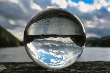 Closeup of a large crystal ball near a lake with the water and sky reflected upside down in it