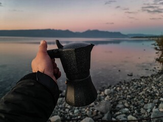 Closeup of a hand holding a thermos against a lake reflecting the pink sky at sunrise