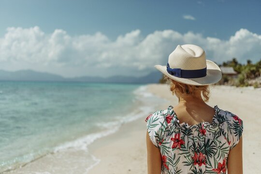 Blonde woman in a summer dress and hat walking on the sandy beach in Romblon, the Philippines