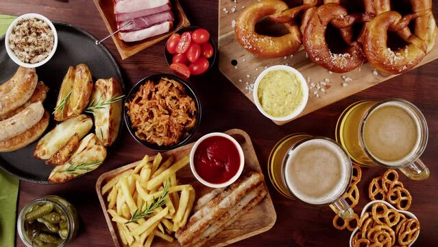 Putting fresh pretzels on table top view. Traditional German Cuisine. Smoked sausages with fried potatoes, beer, pickled cucumbers, bratwursts. Composition of Cooked National Czech Food. 