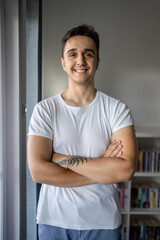 Portrait of one young adult caucasian man stand by the window at home