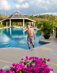 Young men in swim shorts at a pool, men at infinity pool during sunset. man in a swim shorts at the...