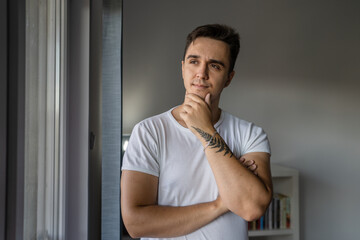 Fototapeta na wymiar Portrait of one young adult caucasian man stand by the window at home