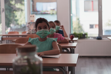 Multiracial group of kids wearing face masks working at class, writing and listening explanations of teacher in classroom